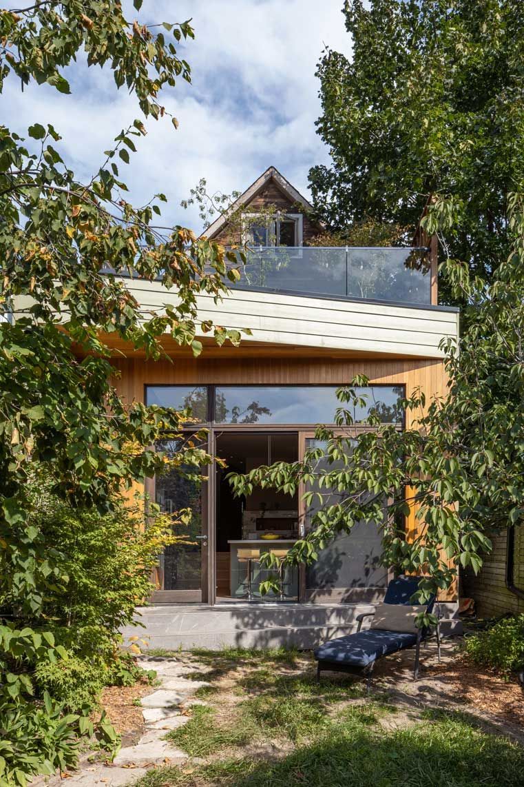 A house with a balcony and a lot of windows is surrounded by trees.