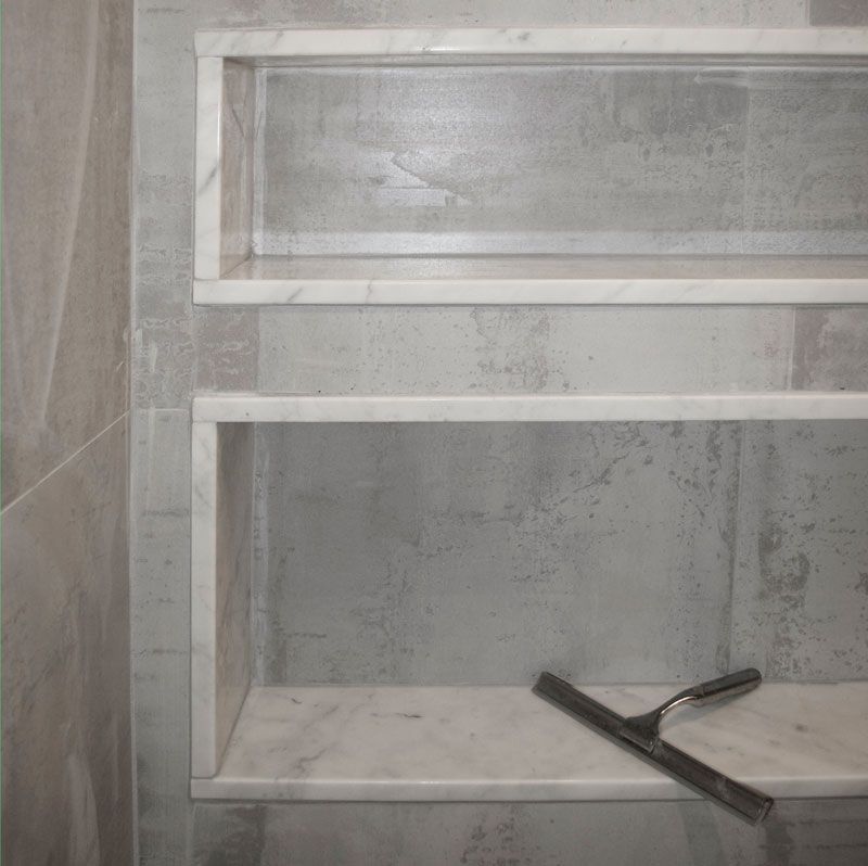 A squeegee is sitting on top of a marble shelf in a bathroom.