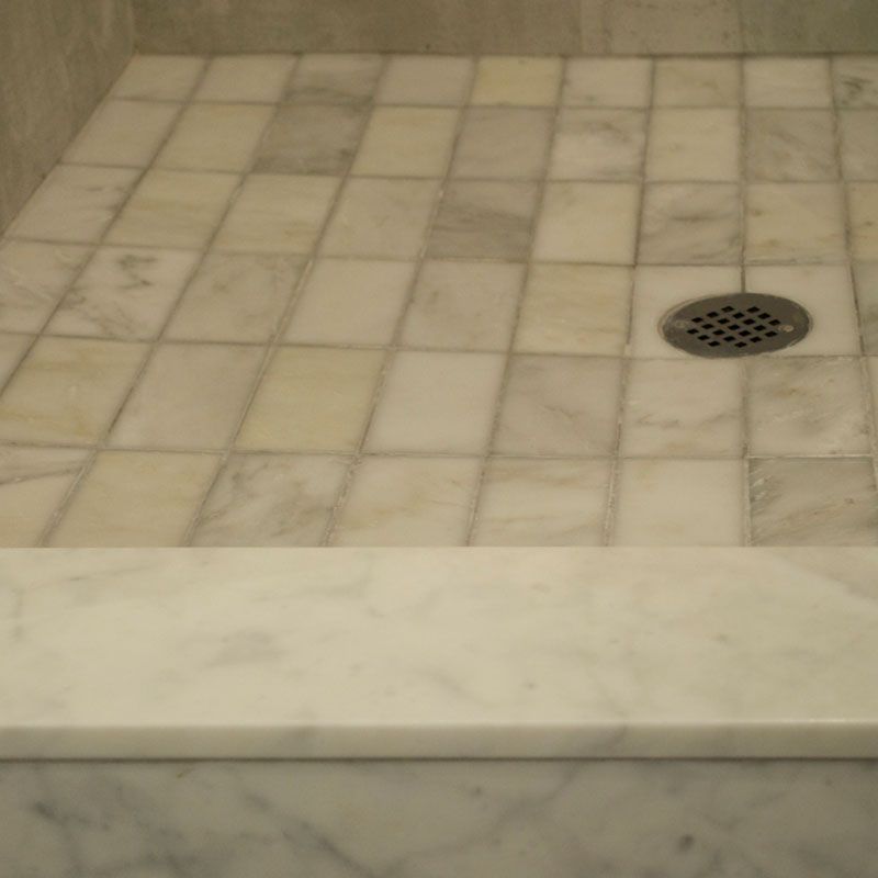 A shower stall with white tiles and a drain on the floor.