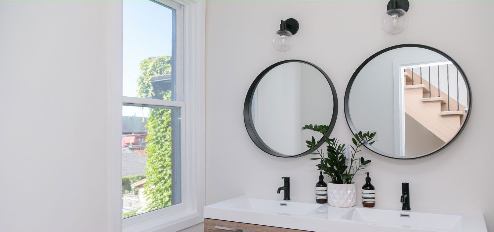 A bathroom with two sinks , two mirrors and a window.