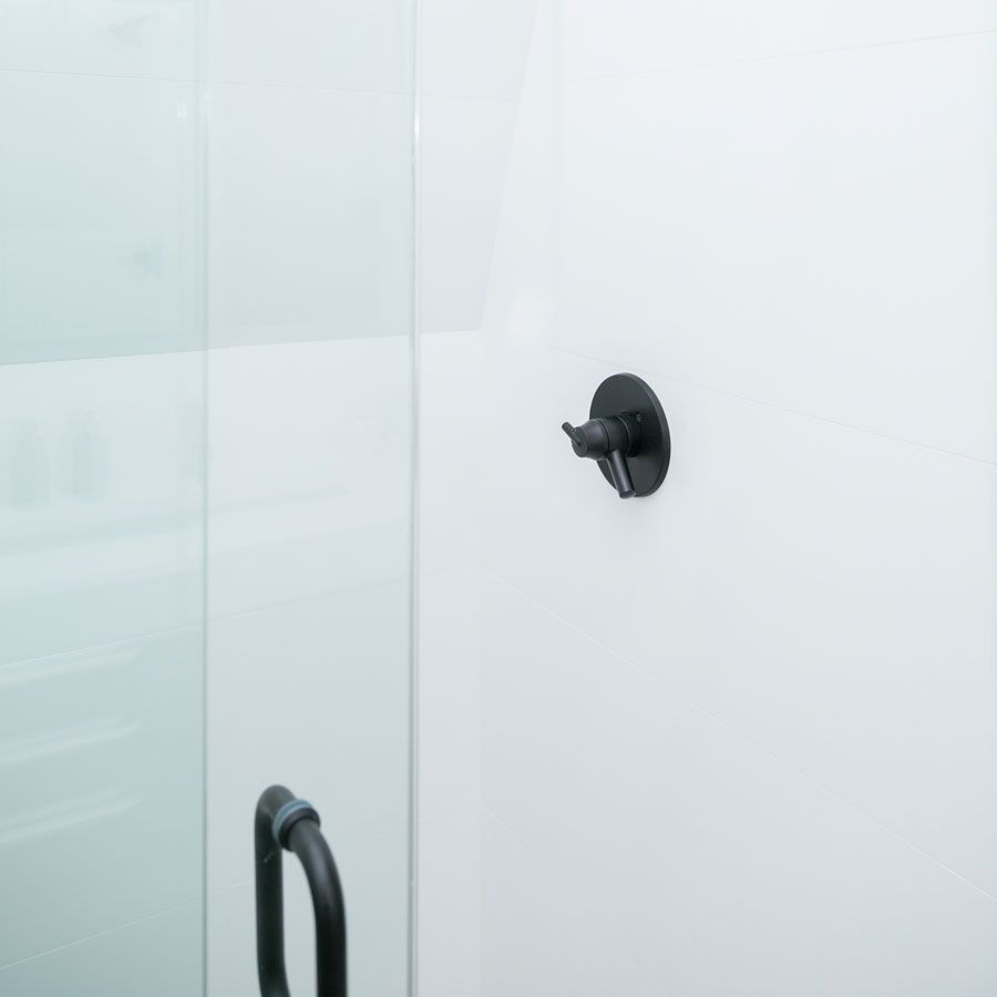 A black shower head is hanging on a white wall next to a glass shower door.