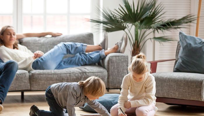 A family is sitting on a couch in a living room while two children are playing on the floor.