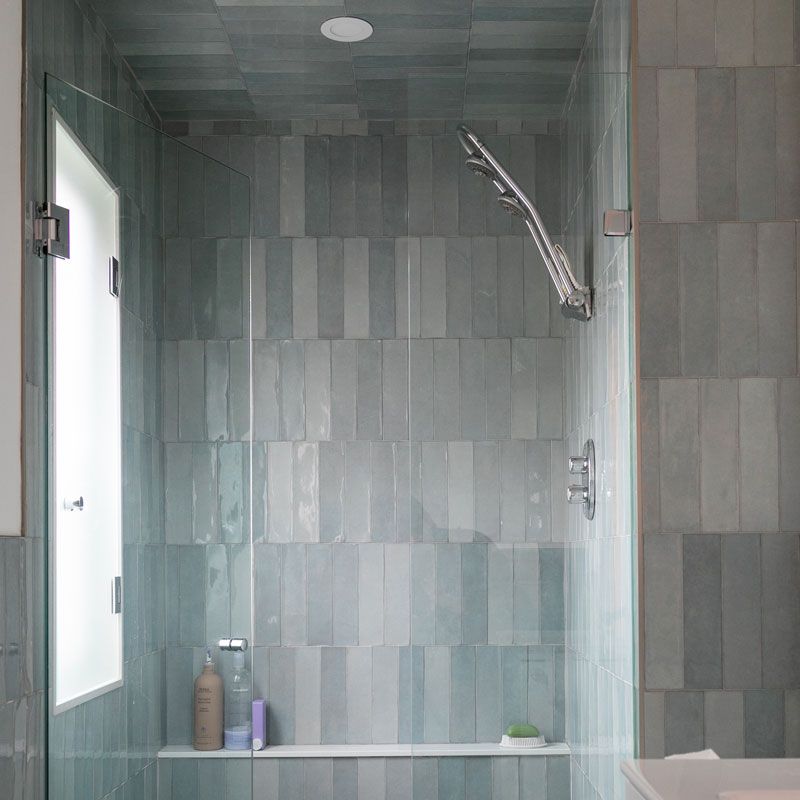 A bathroom with a walk in shower with a glass door and a window.