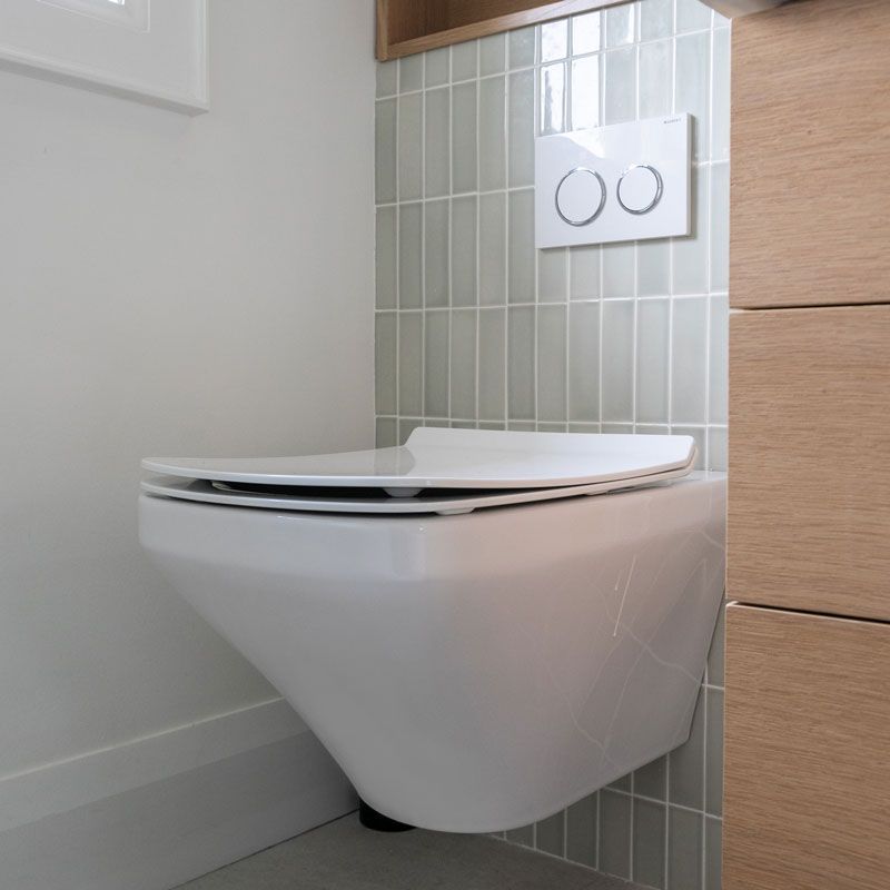 A white toilet is mounted to the wall in a bathroom.