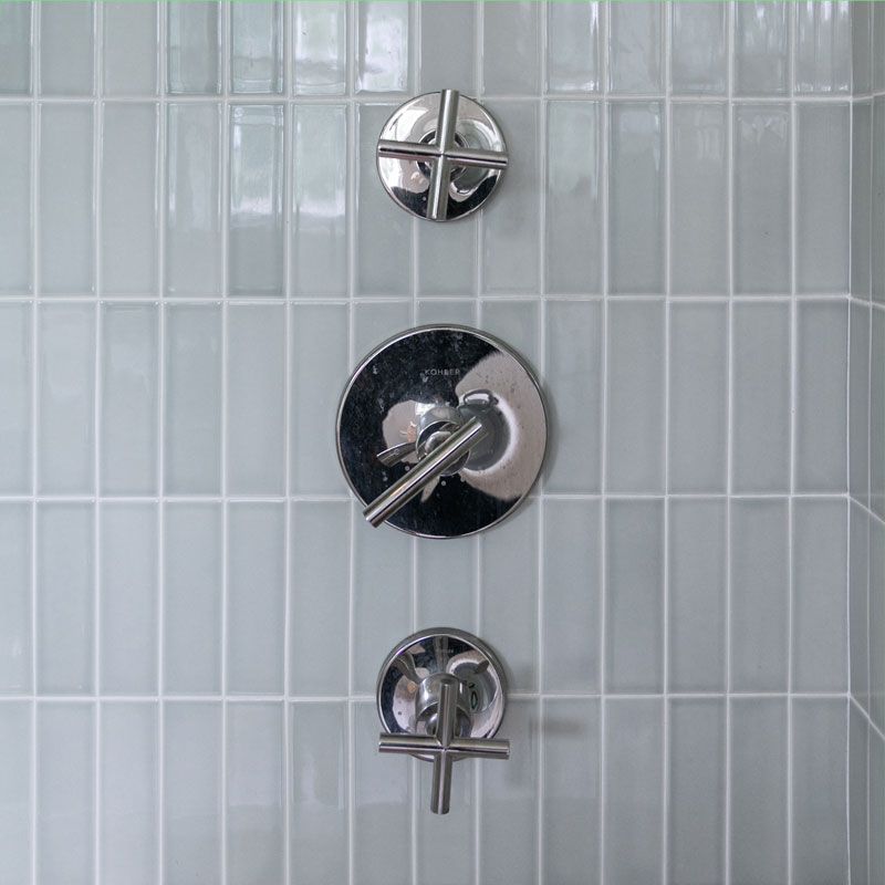 A close up of a shower head with three faucets on a tiled wall.