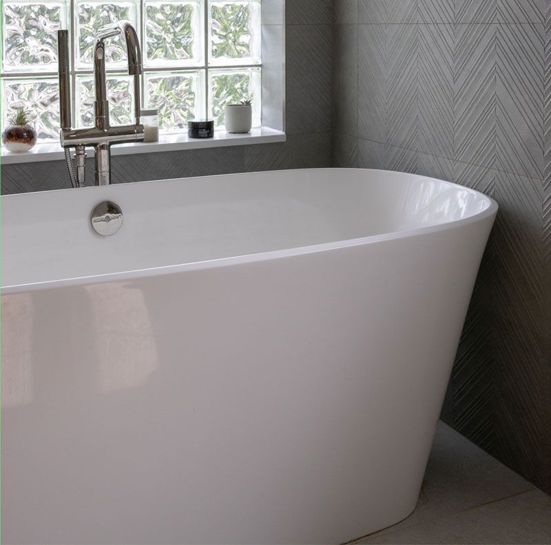 A white bathtub is in a bathroom next to a window