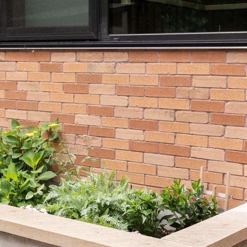 A brick wall with a window and a planter with plants in front of it