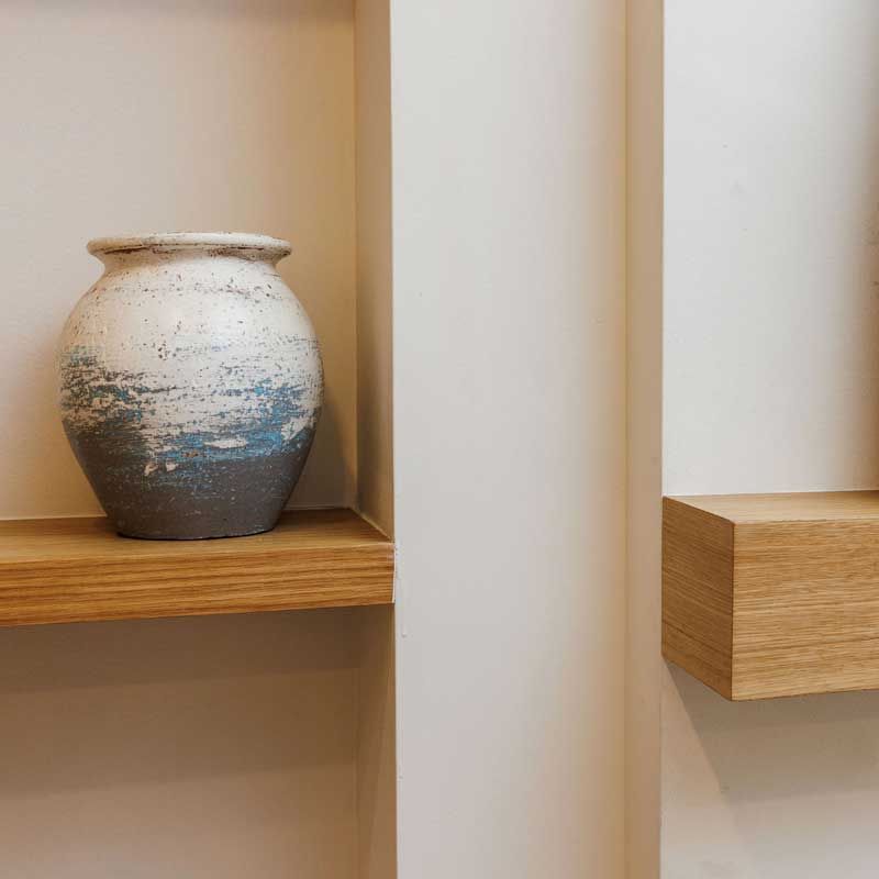 A vase is sitting on a wooden shelf next to a wall.