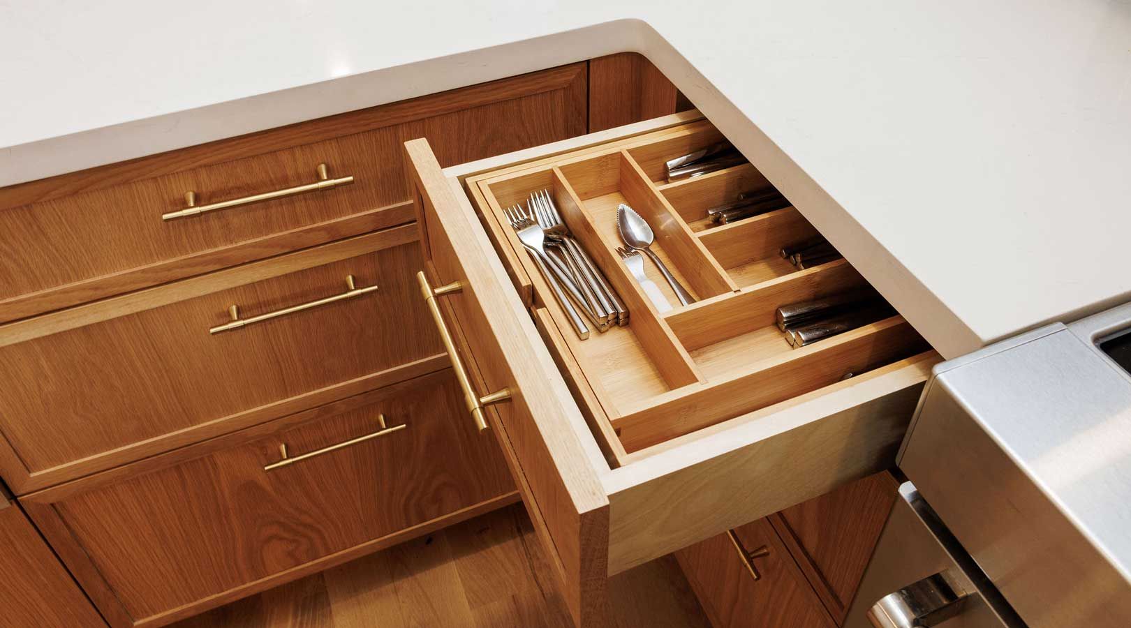 A kitchen with wooden cabinets and a drawer filled with silverware.
