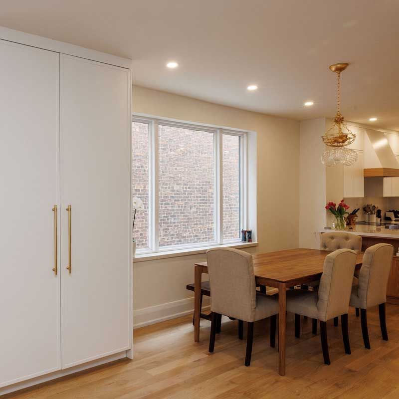 A dining room with a wooden table and chairs and a large window.