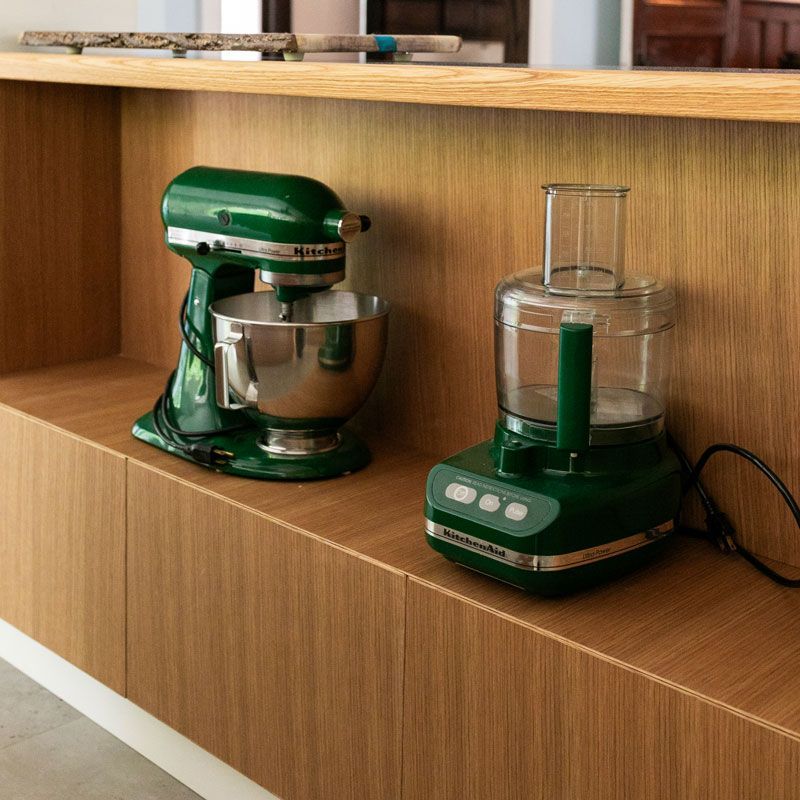 A green kitchenaid mixer and a green food processor on a wooden shelf