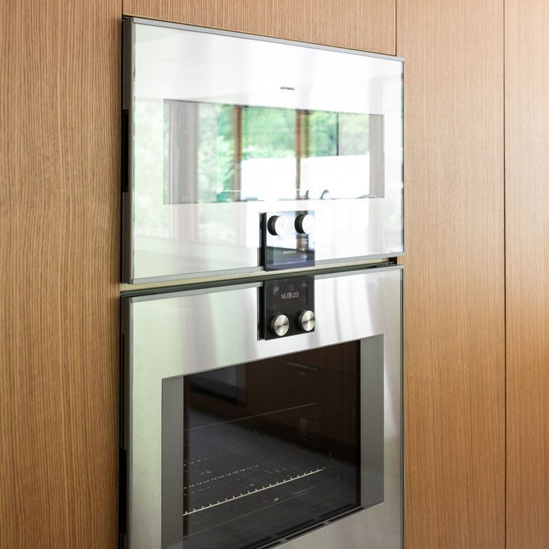 A stainless steel oven is mounted to a wooden wall.