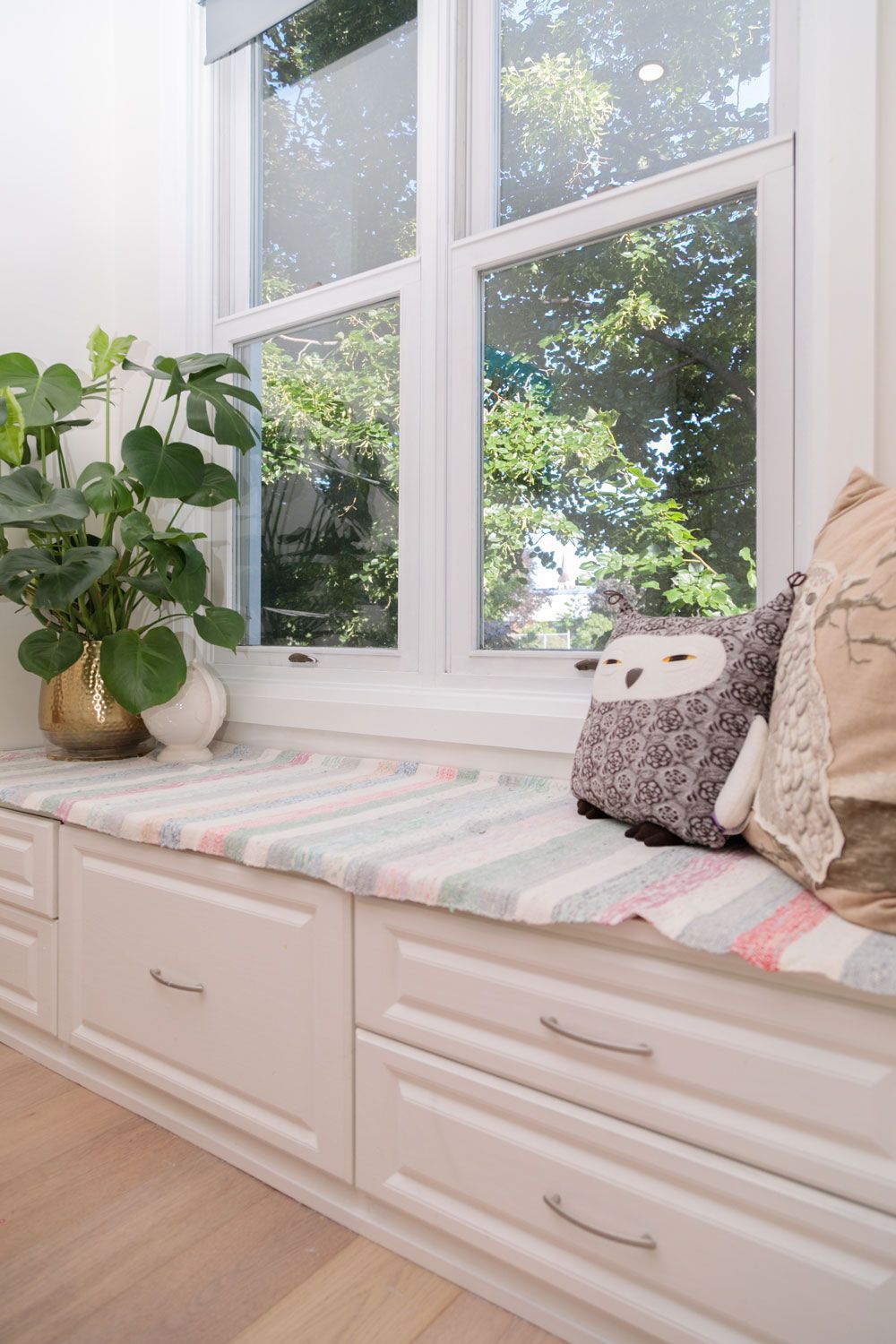 A window seat with pillows and a plant in a room.