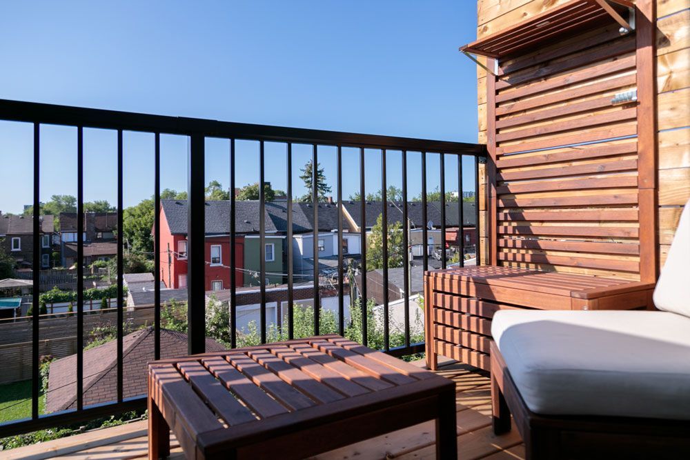 A third-story balcony with a chair, table, and ottoman with a view of a residential area.