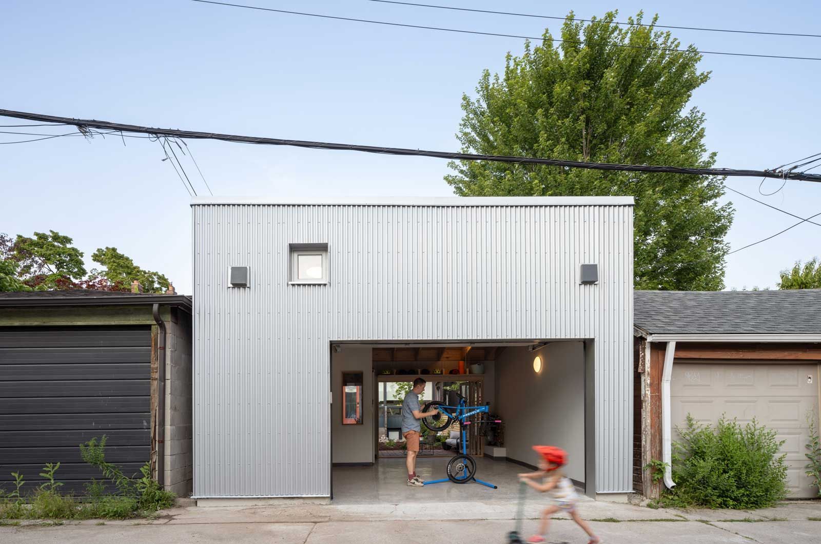 A little girl is riding a scooter in front of a garage.