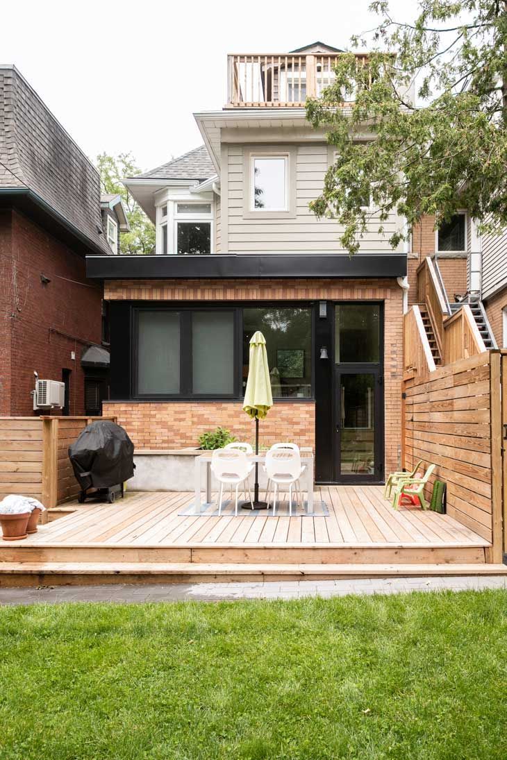 The backyard of a house with a wooden deck and umbrella.