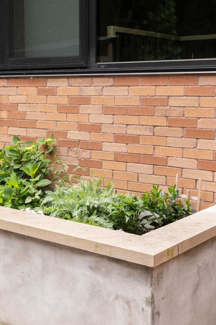 A brick wall with a window and a planter with plants in front of it.