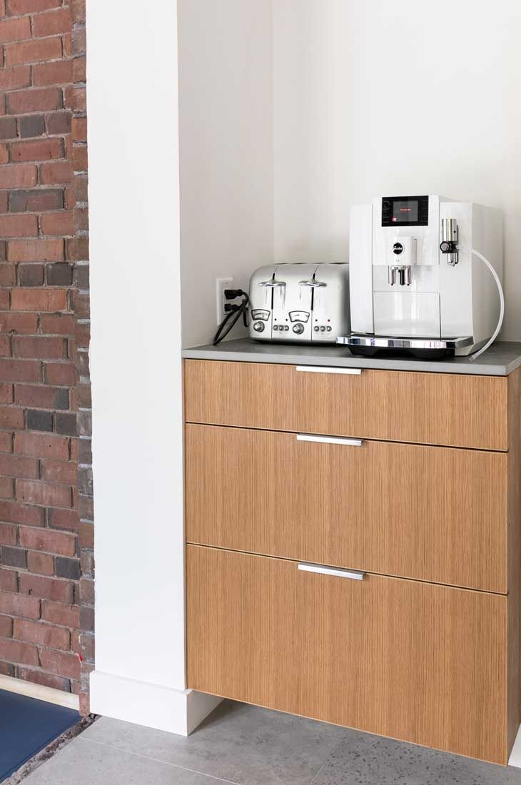A toaster and a coffee maker are on a wooden cabinet in a kitchen.