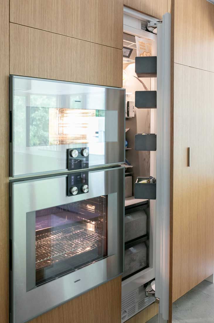 A stainless steel oven is built into a wooden wall next to a refrigerator.