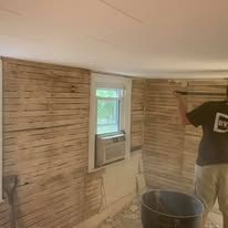 A man is standing in a room with wooden walls and a window.