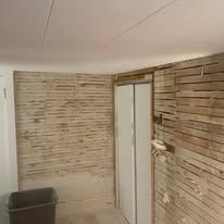 A room with a wooden wall and a trash can in it.