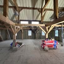 A large empty room with wooden beams and a stack of bags on the floor.