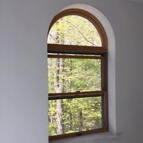 A large arched window with a view of a forest.