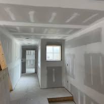 A hallway with drywall walls and a window in a house under construction.