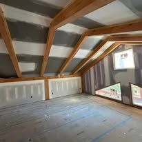 A room with a ceiling made of drywall and wooden beams.