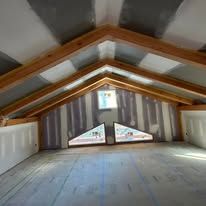 An empty attic with a vaulted ceiling and two windows.