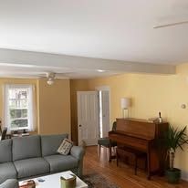 A living room with a couch , piano , and ceiling fan.