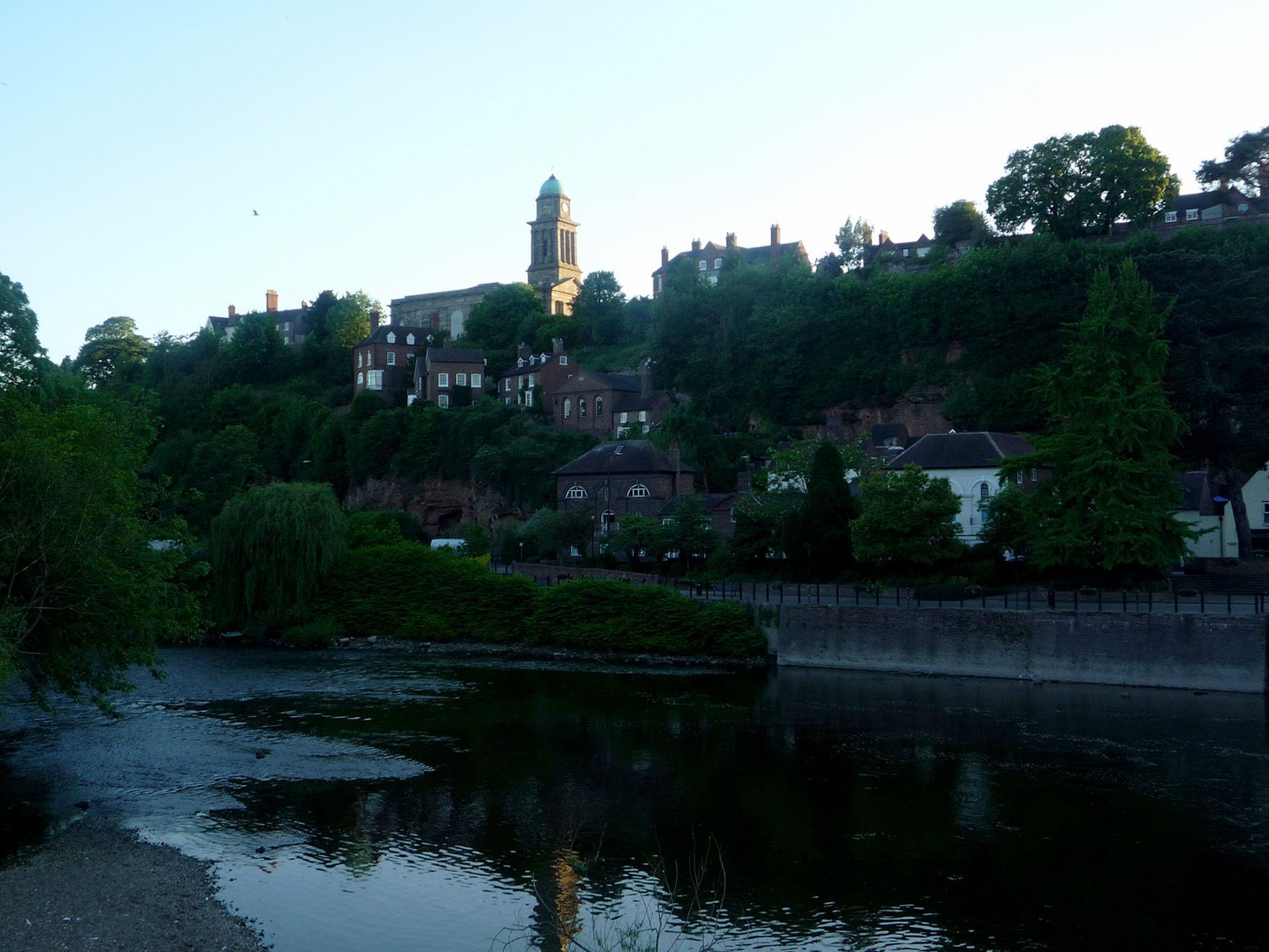 A river surrounded by trees and buildings with a clock tower in the background