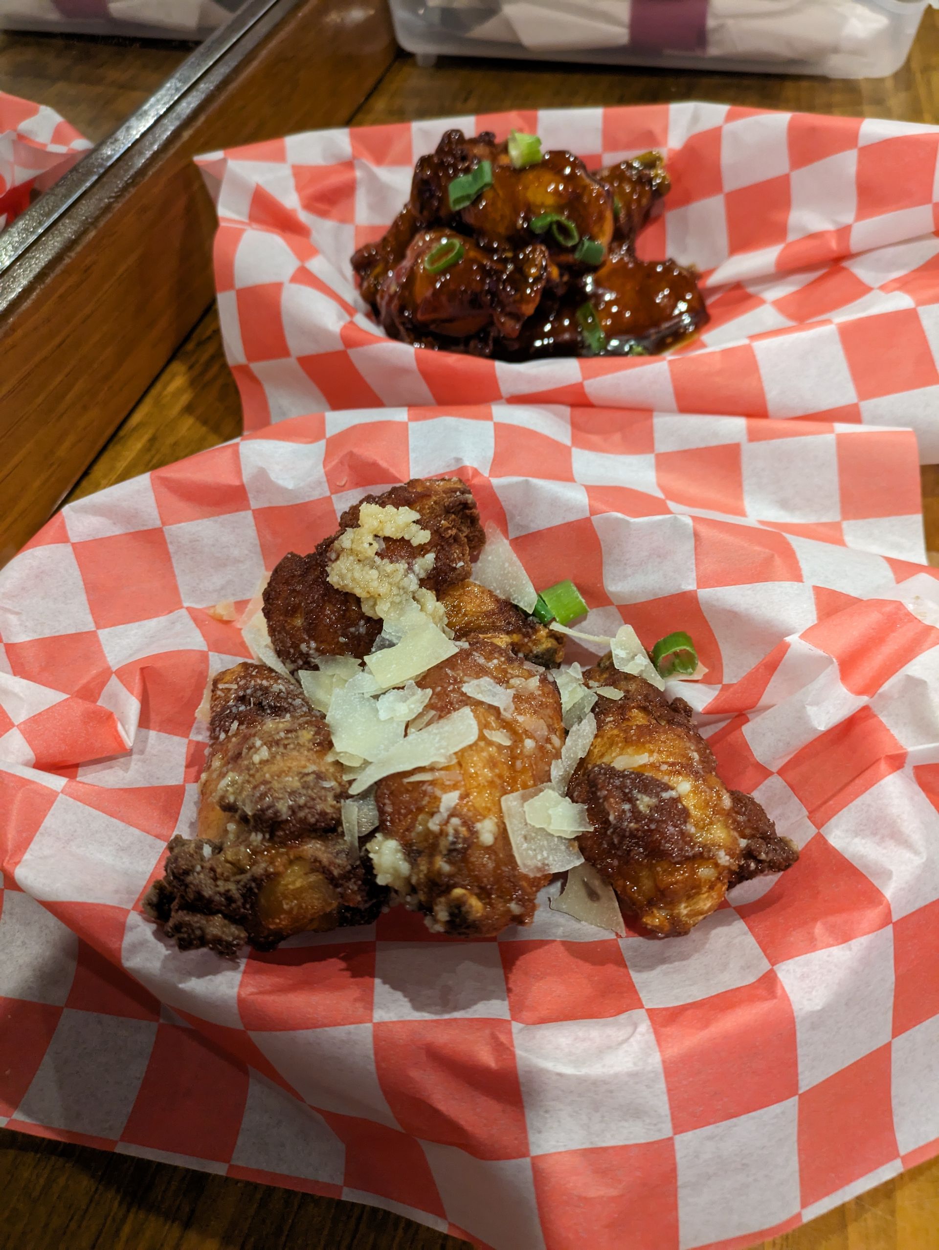 Two plates of chicken wings on checkered paper on a table.