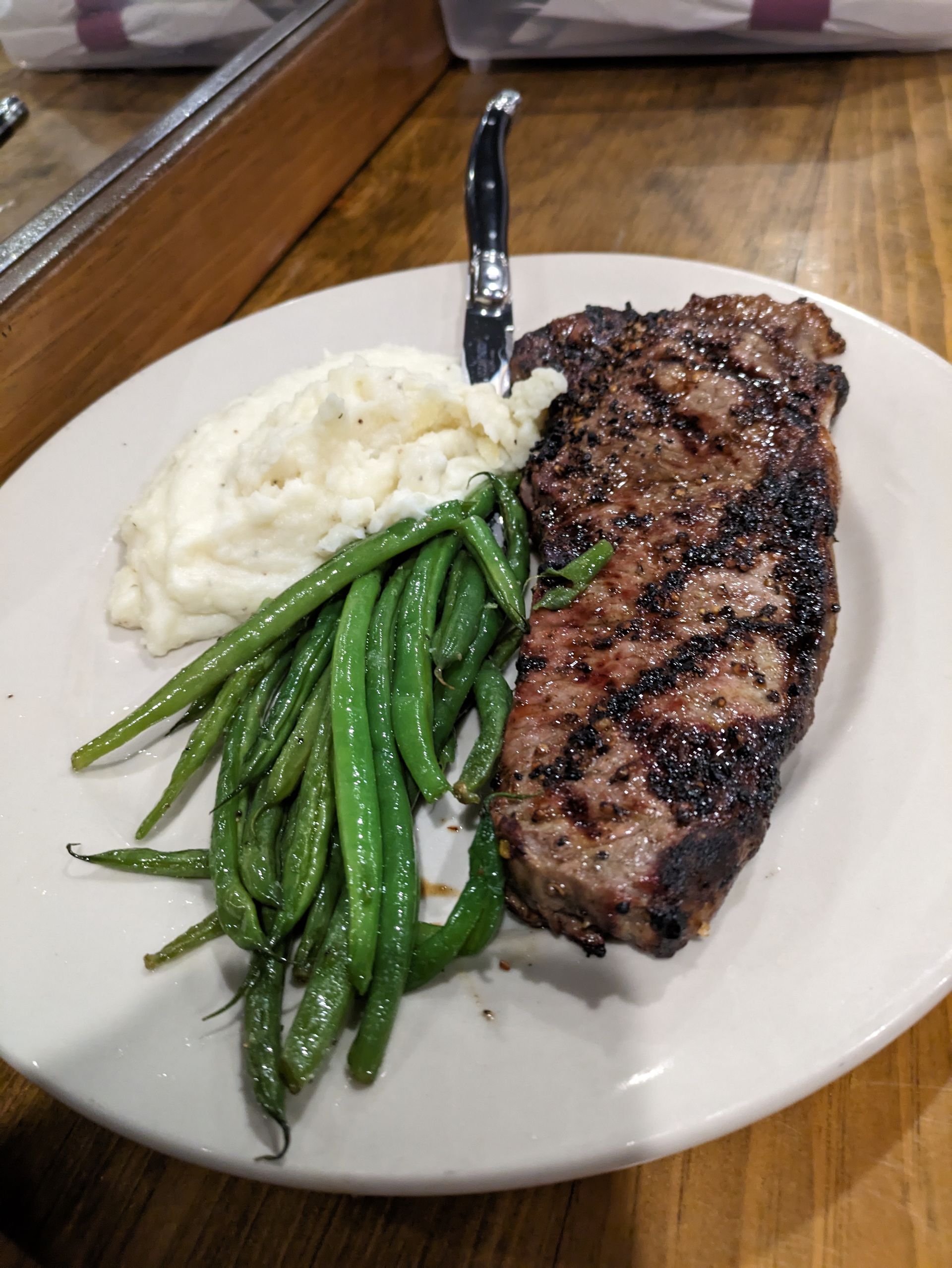 A white plate topped with a steak , green beans and mashed potatoes.