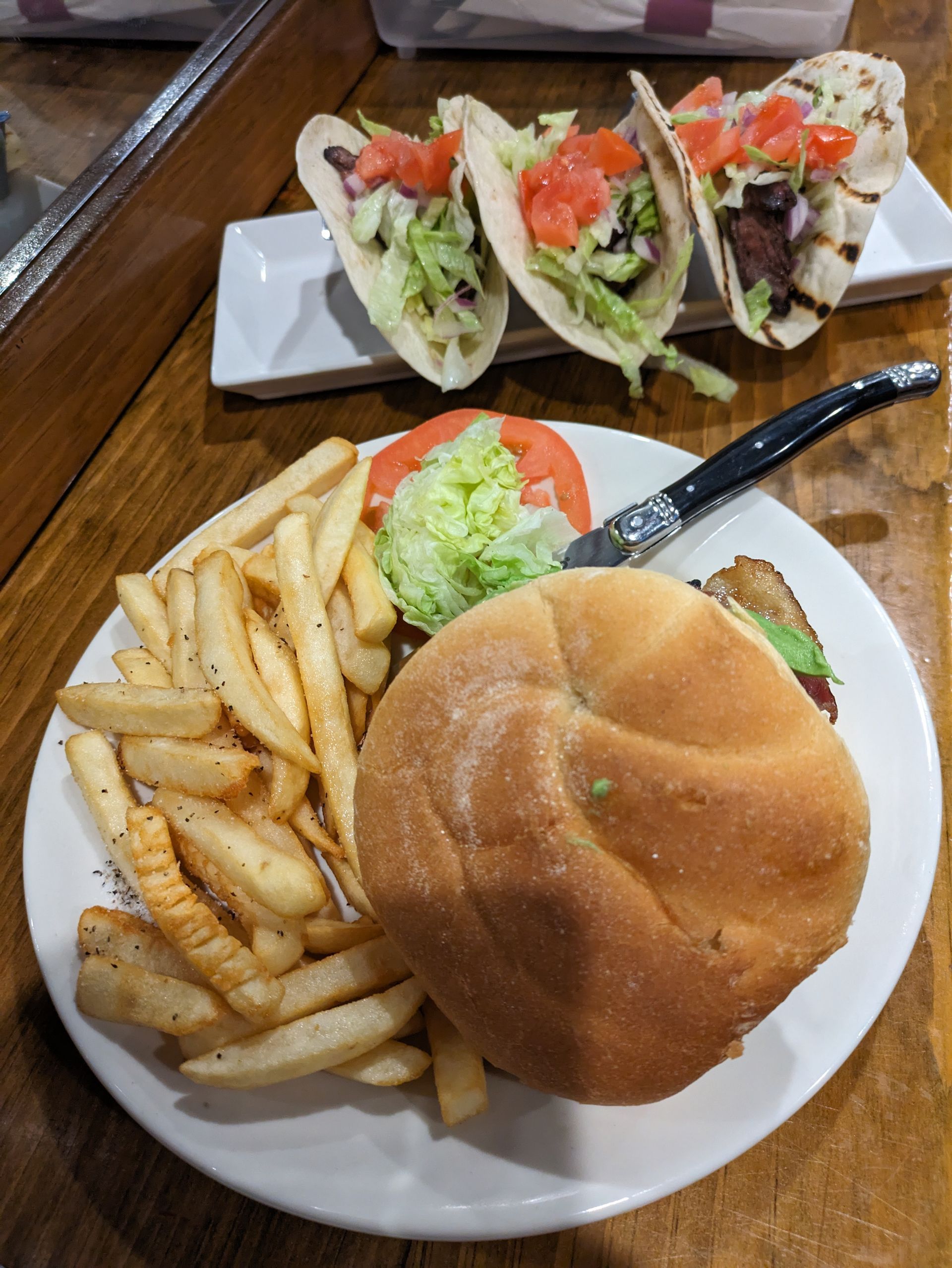 A plate of food with a hamburger, french fries and tacos on a table.