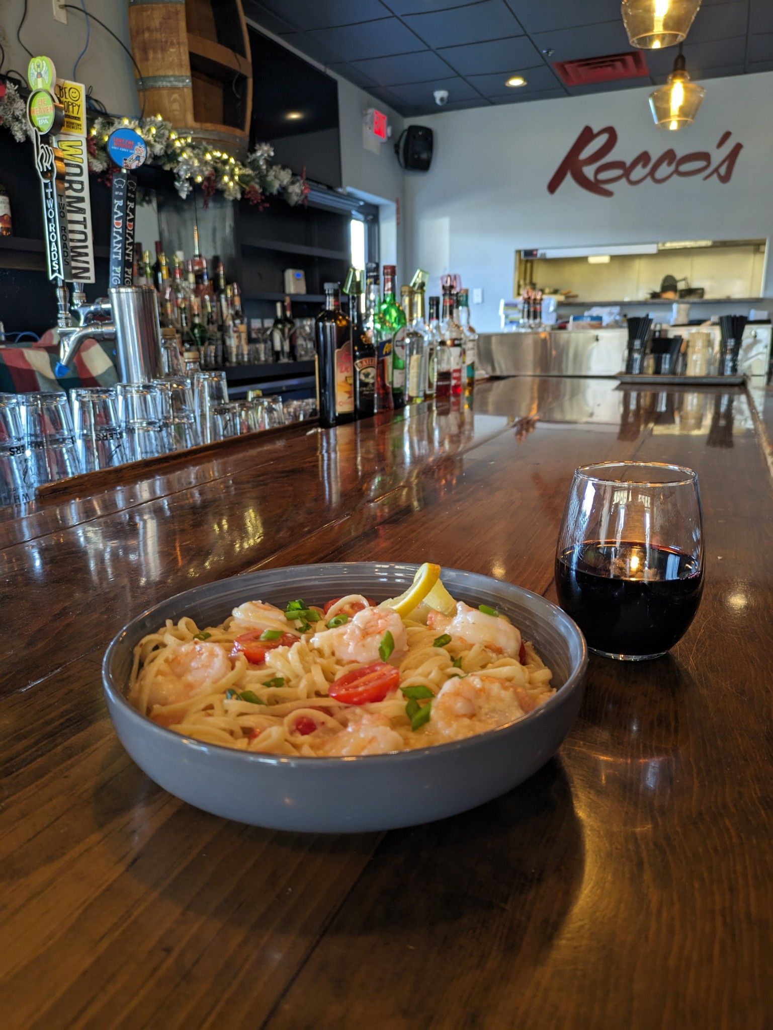 A bowl of food is sitting on a wooden table next to a glass of wine.