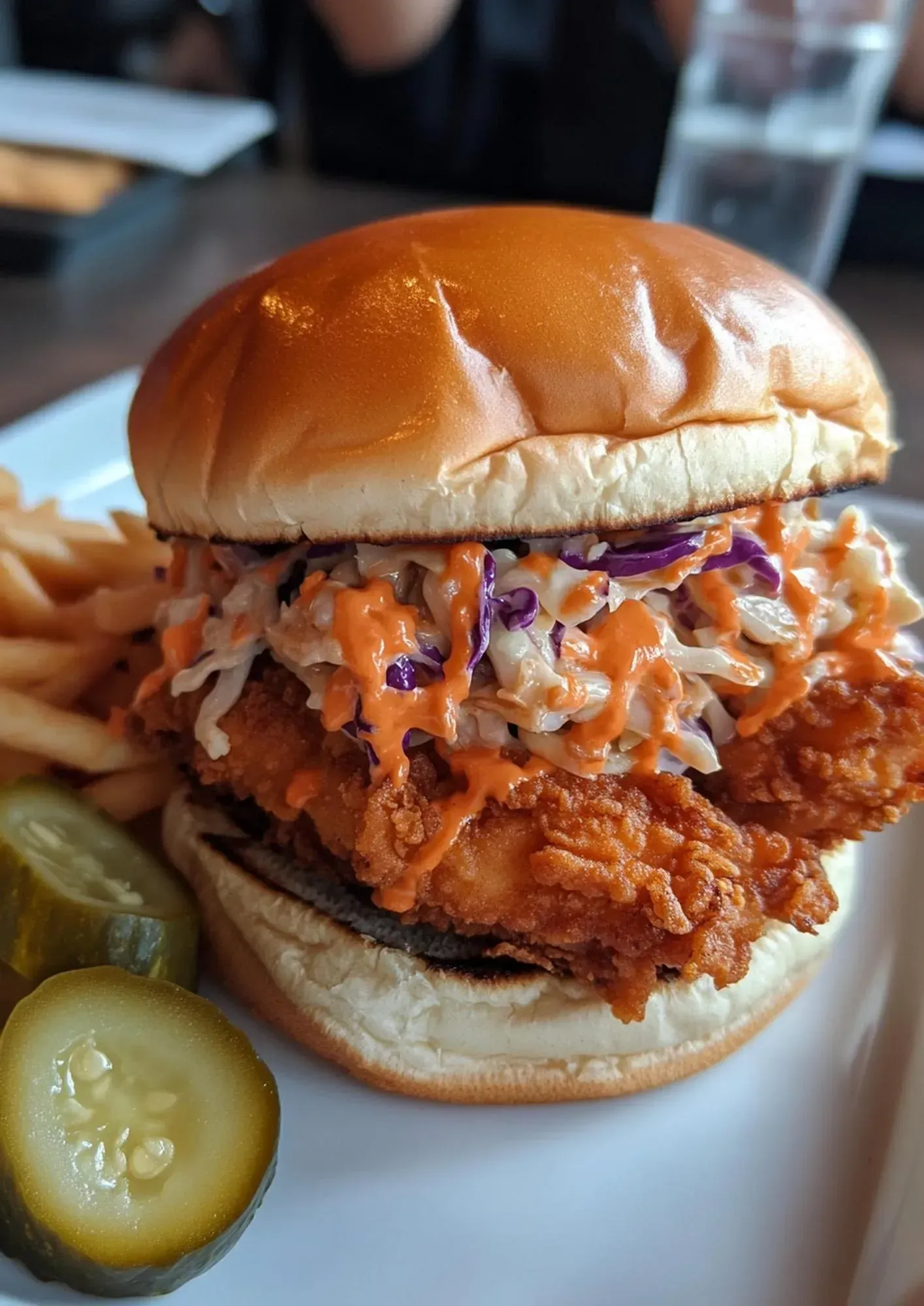 A close up of a fried chicken sandwich with coleslaw and french fries on a plate.