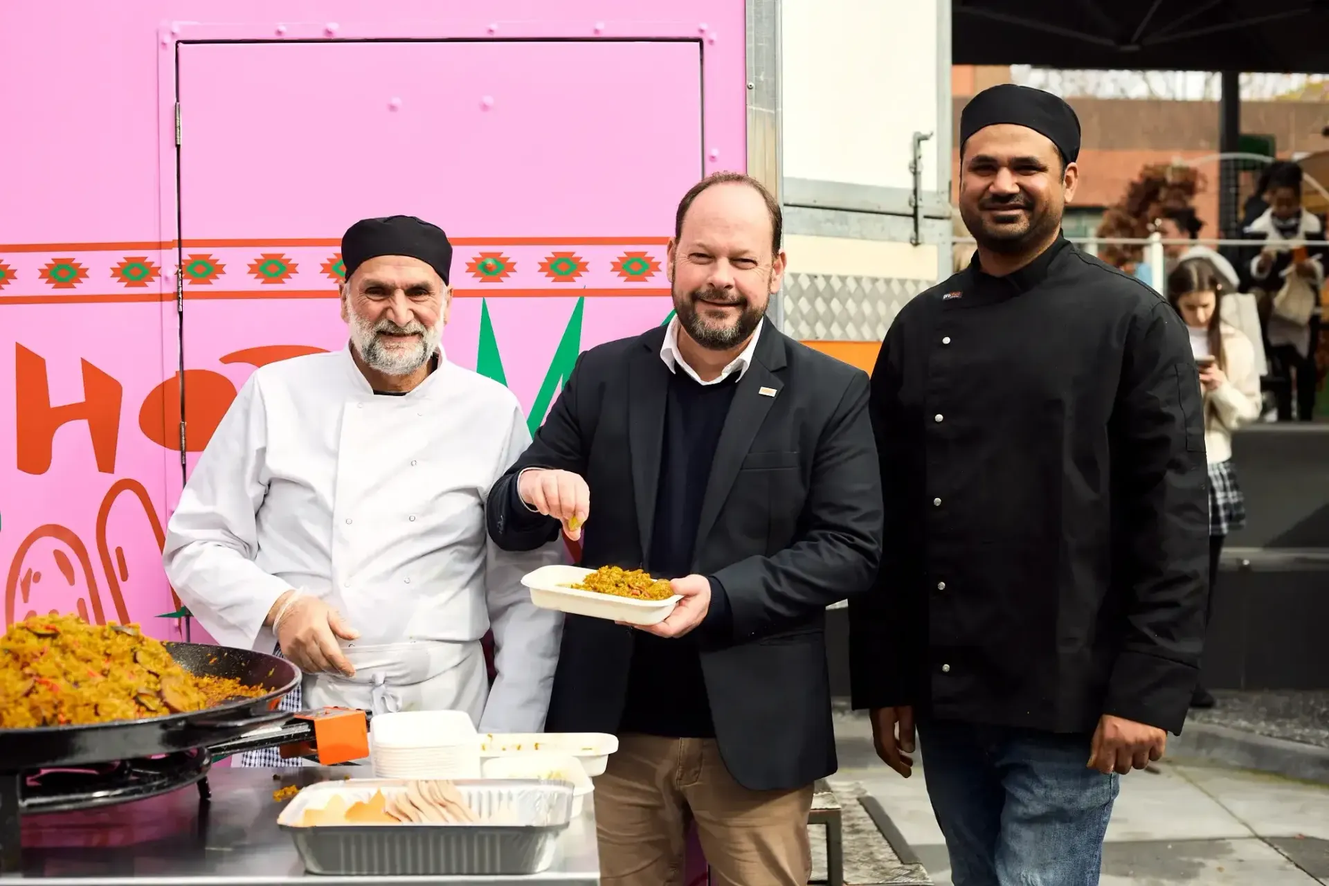 Three men are standing next to each other holding plates of food from Food truck.