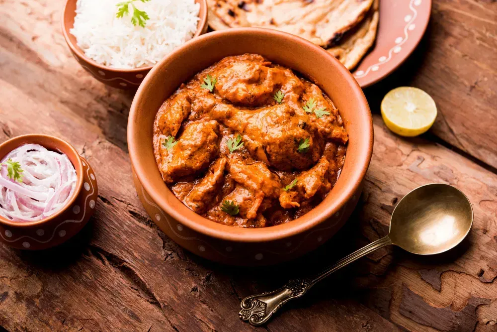 A bowl of chicken curry with rice and roti on a wooden table.