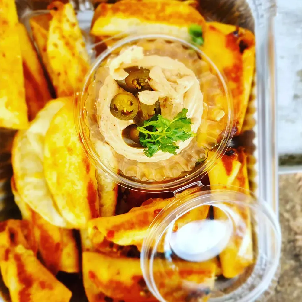 A close up of a tray of food with a bowl of dip on top.