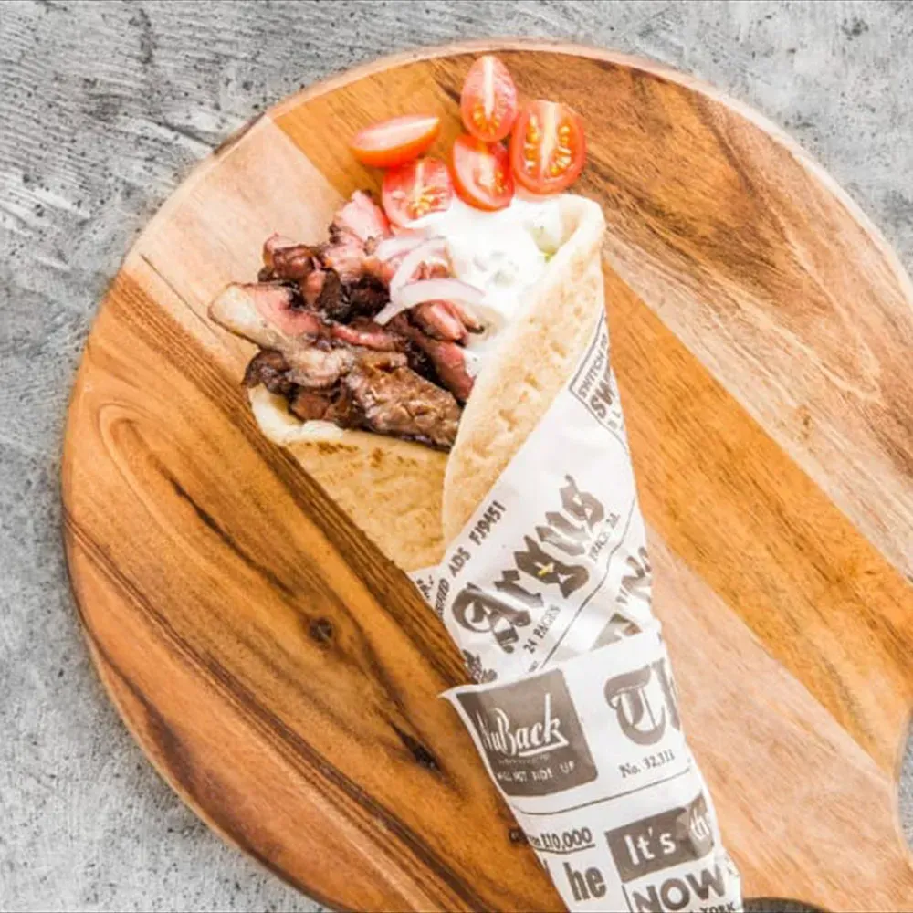A wrap with Souvlaki meat and tomatoes on a wooden cutting board