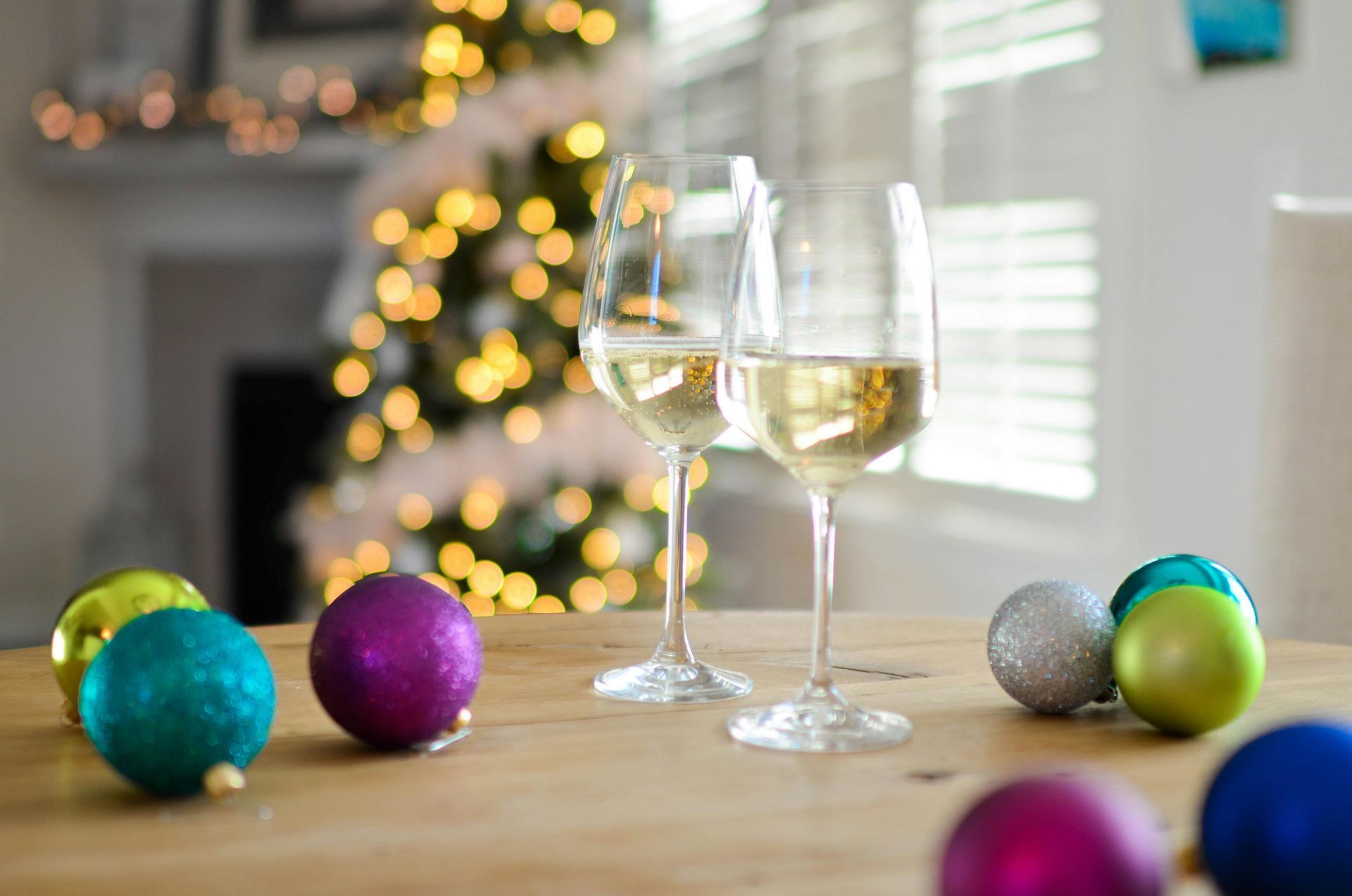 Two glasses of wine are sitting on a wooden table with christmas decorations.