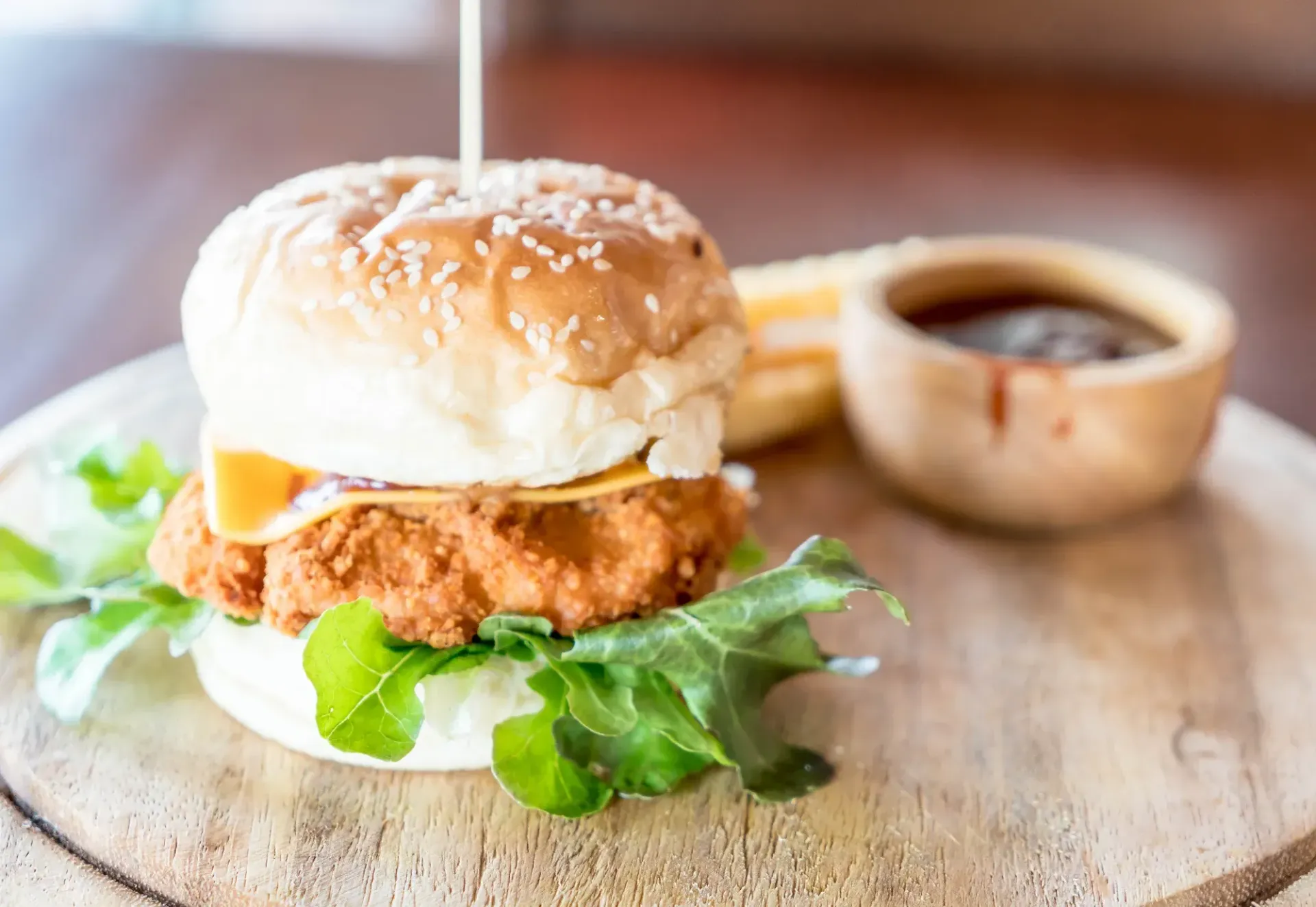 A close up of a chicken burger on a wooden cutting board.