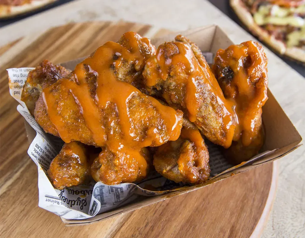 A tray of chicken wings with buffalo sauce on a wooden table.