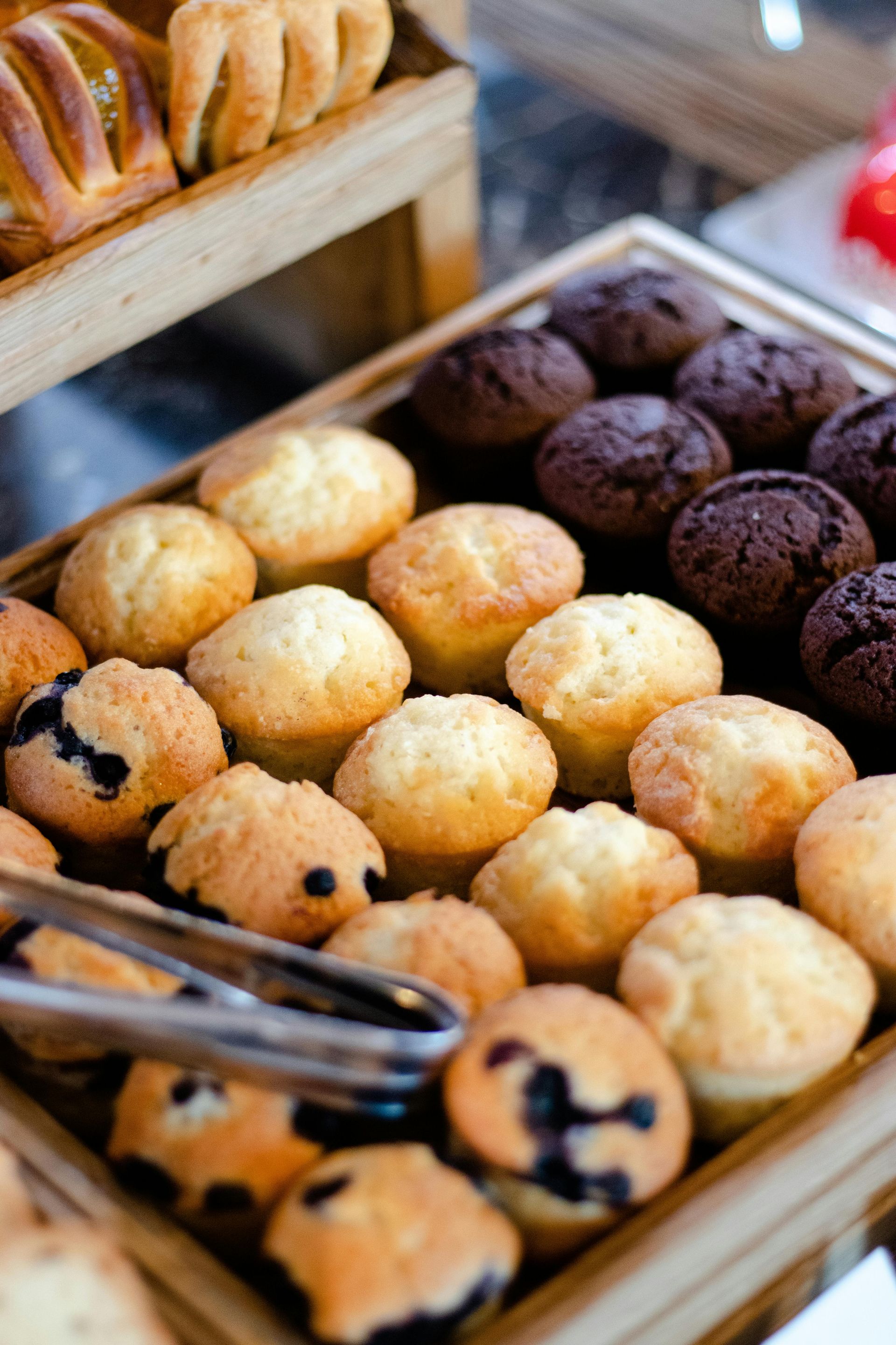 A wooden box filled with muffins and tongs on a table for a party catering service.
