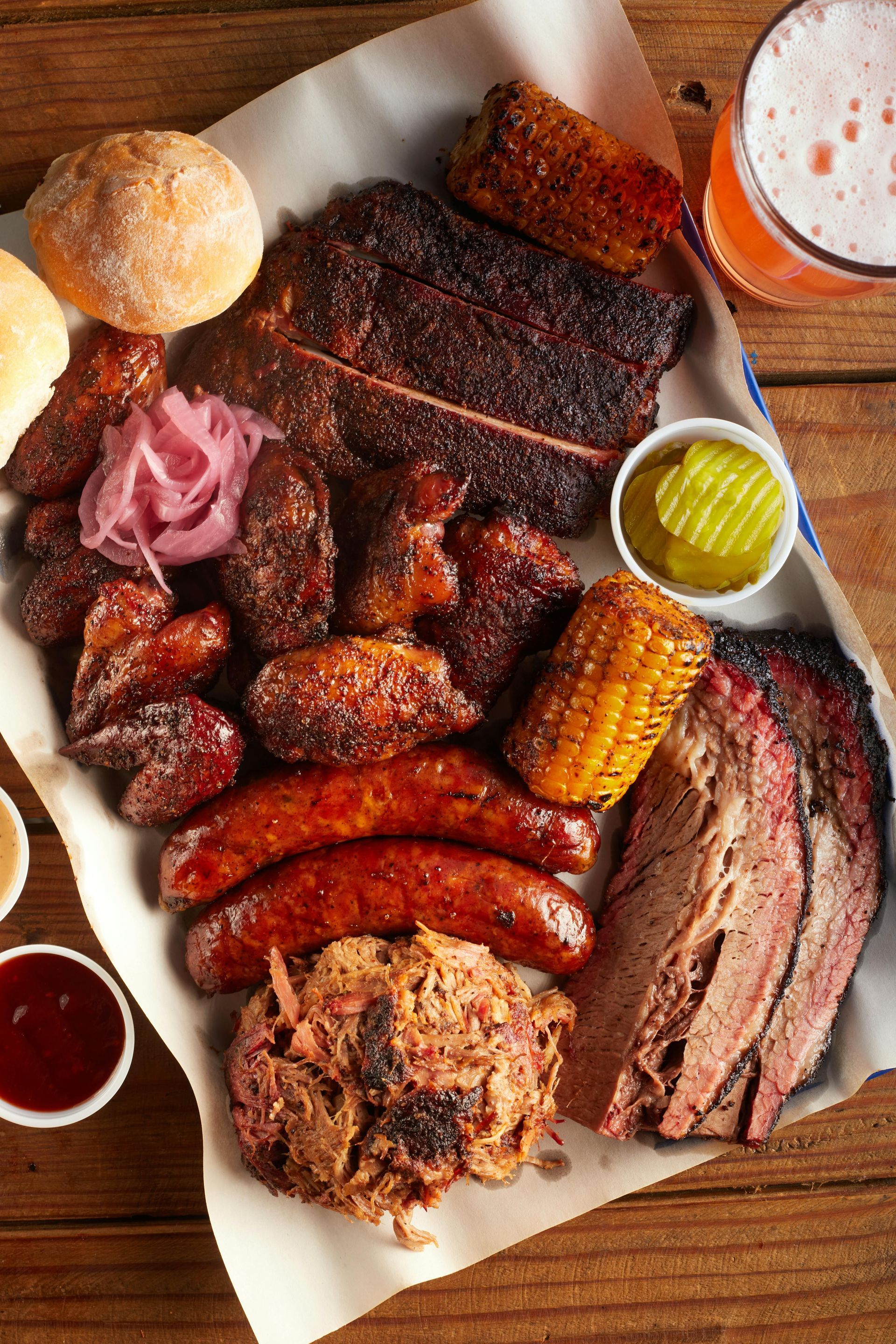 A large platter of barbecue meats and sauces on a wooden table.