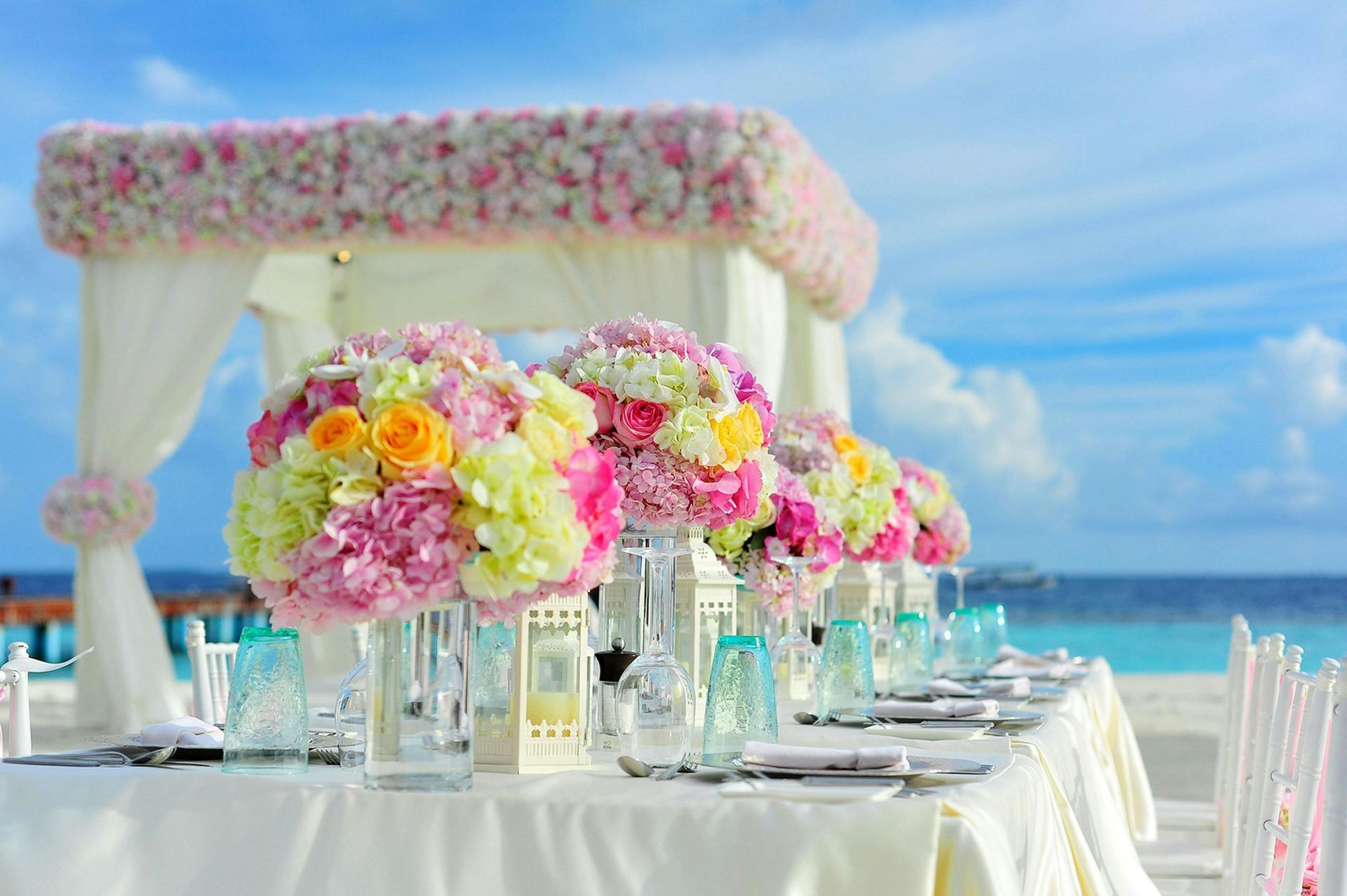 A table set for a wedding reception on the beach with flowers on it.