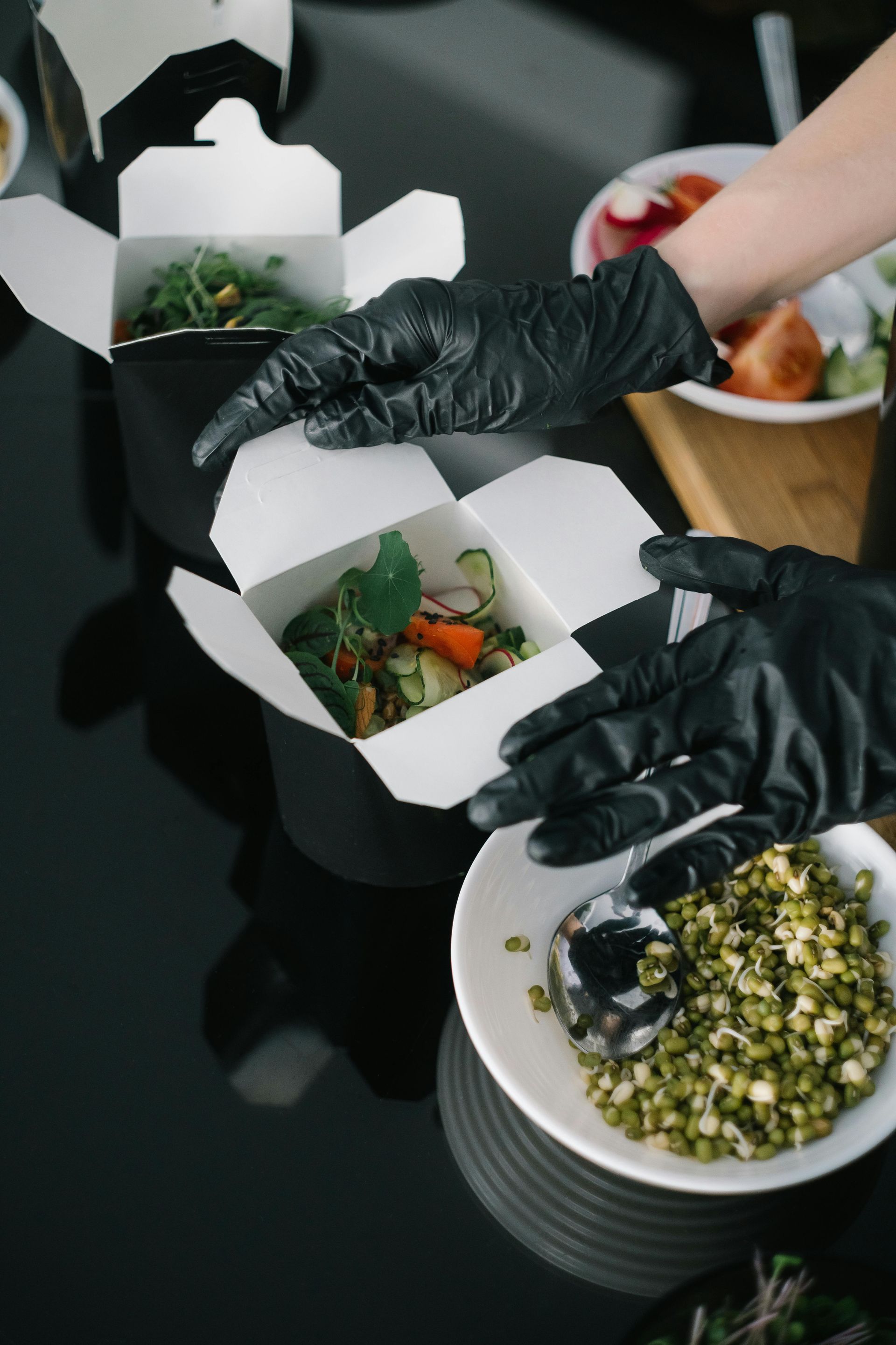 A person wearing black gloves is holding a box of food and a bowl of food.