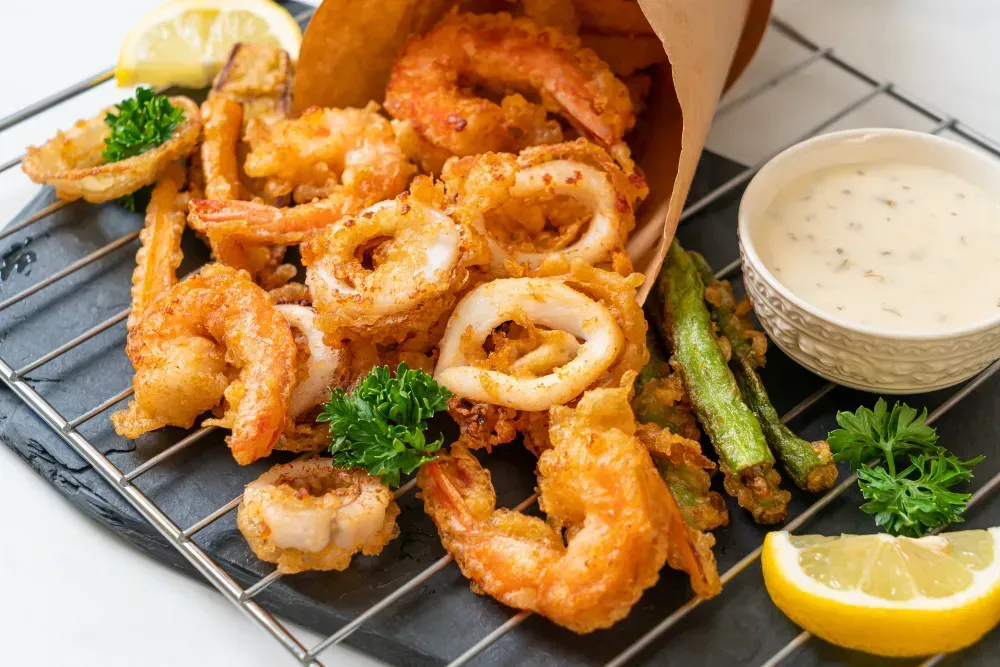 A bag of fried prawns, shrimp , squid , and asparagus on a wire rack.