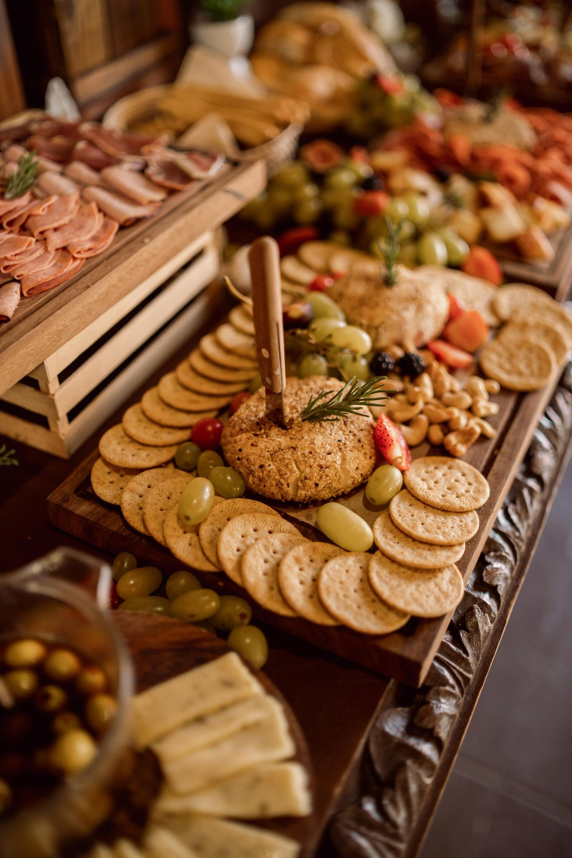 A wooden table topped with a variety of food including crackers , grapes , nuts and cheese.